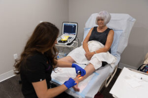 A woman with short hair sits on a treatment chair and receives non-surgical vein treatment in Lakewood Ranch from one of our providers.