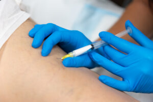 A pair of hands in medical gloves perform an injection for varicose and reticular vein treatment in Lakewood Ranch.