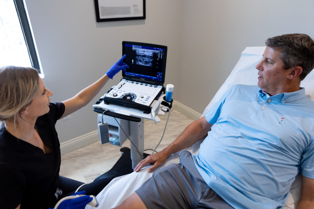 A male patient watches as a provider points to a vein ultrasound screen, showing him his vein issue. This helps to choose the right saphenous vein treatment in Lakewood Ranch.